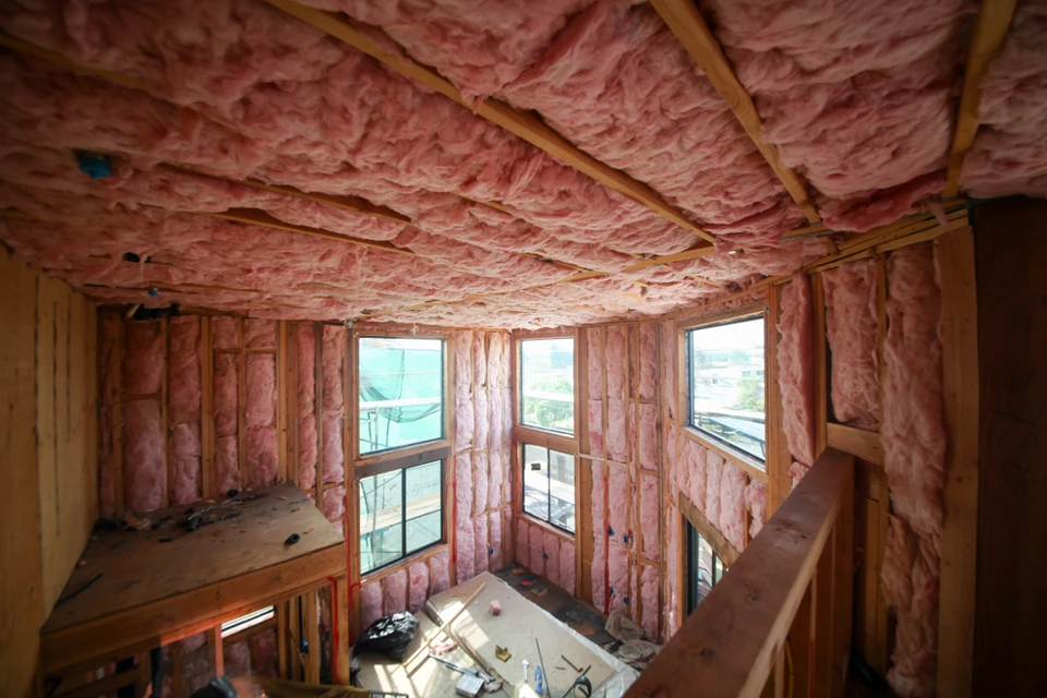 Chantier de construction résidentielle en cours, structure bois avec isolation thermique rose entre montants et solives apparentes