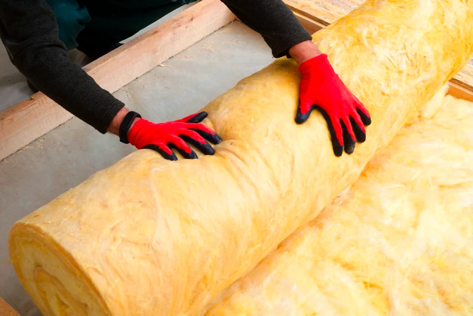 Ouvrier de construction caucasien avec rouleau de matière isolante, plancher isolant par laine minérale